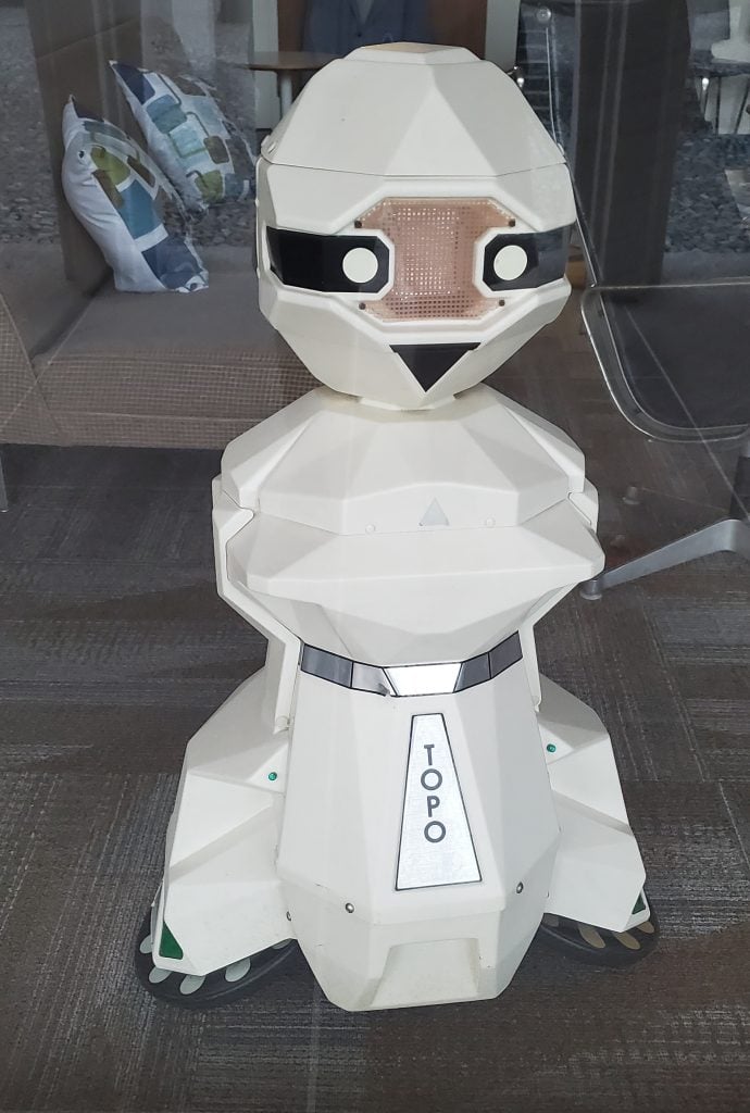 Front view of a white TOPO robot with a geometric design, black visor, and the name 'TOPO' displayed on its front panel.